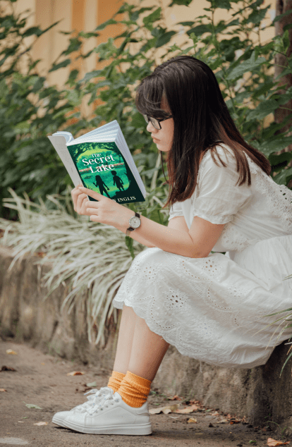 Girl sitting and reading The Secret Lake by Karen Inglis